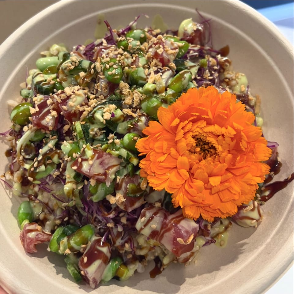 Benicia Poke Co's poke bowl with tuna, edamame, sauces, and an orange flower garnish.
