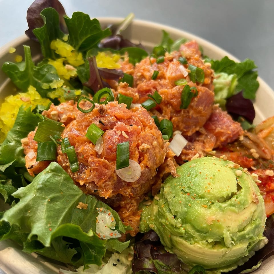 A vibrant Benicia Poke Co. poke bowl with salmon, avocado, kimchi, and green onions.