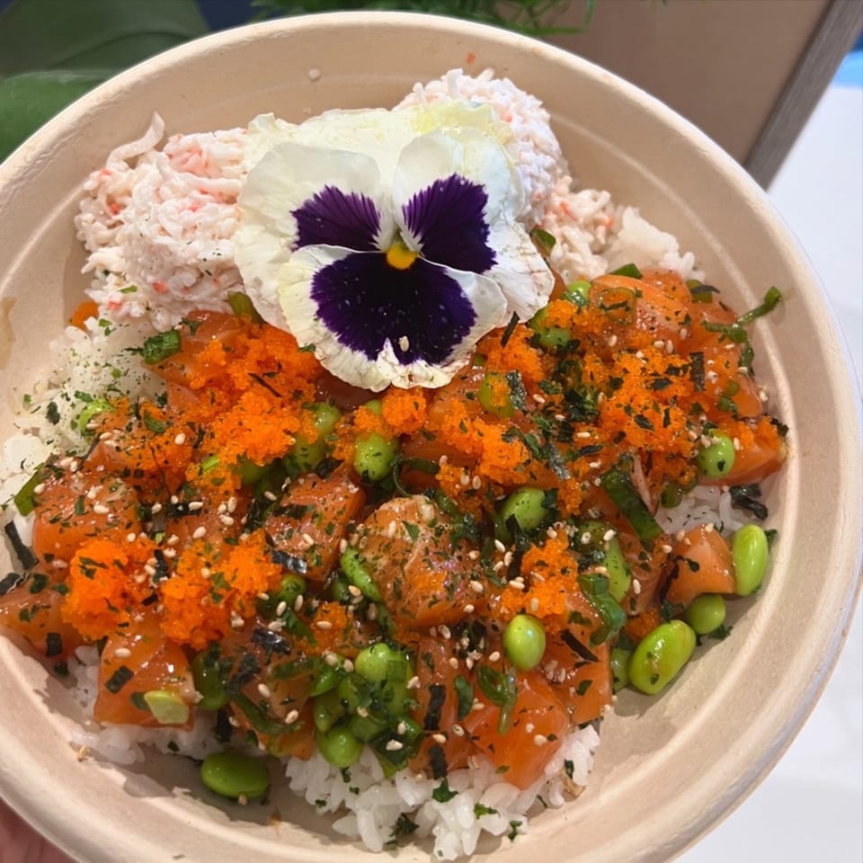Benicia Poke Co. poke bowl with salmon, edamame, roe, and crab salad, garnished with a pansy.